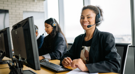 A person smiling sat at their computer and wearing a mic.