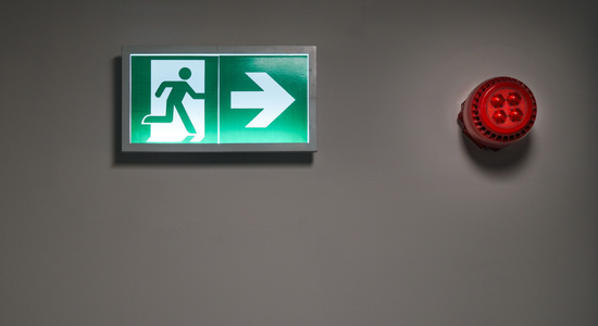 A green emergency exit sign next to a red alarm.png