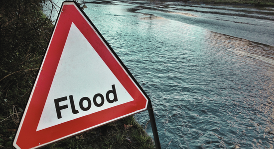 A red triangle sign that warns that there is flooding on a open road